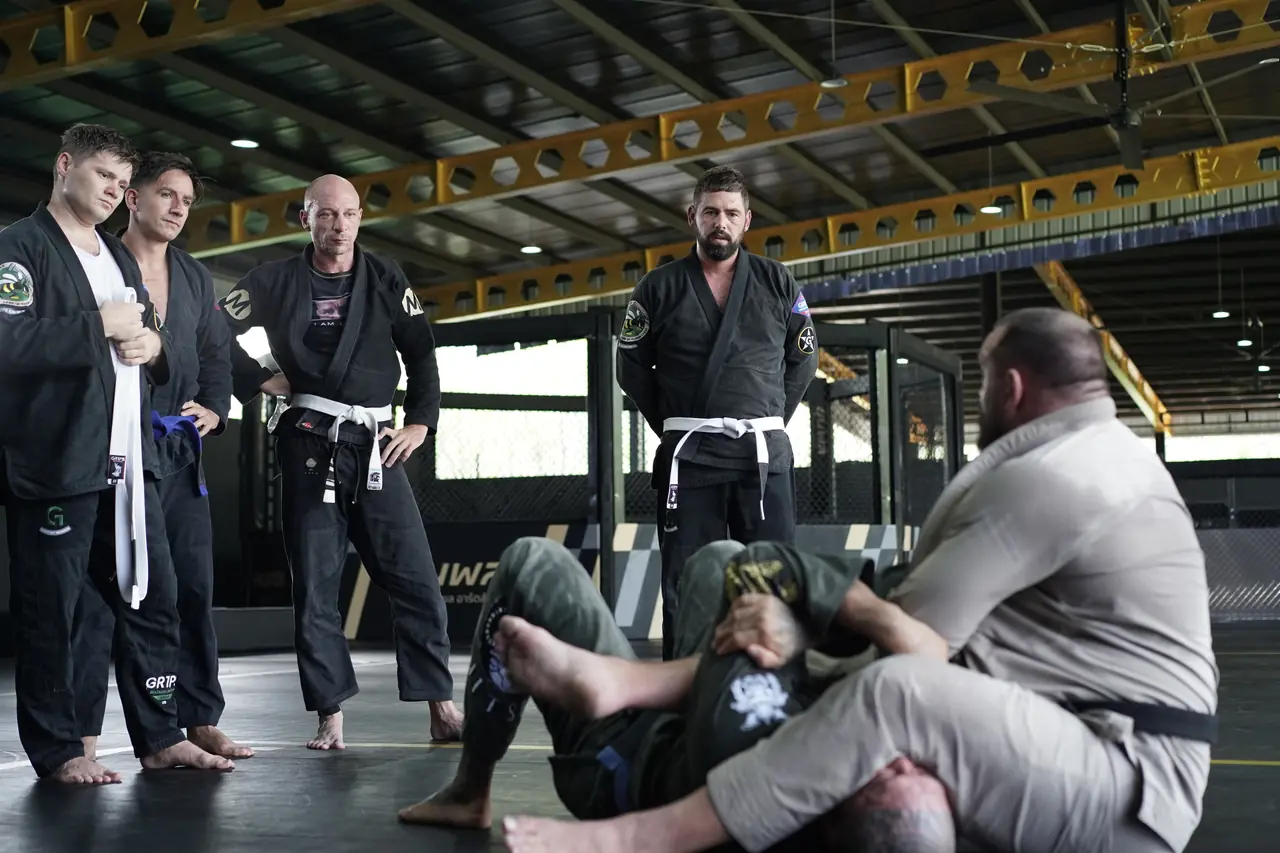 A coach demonstrates a position on the mat while students in gis and coloured belts watch