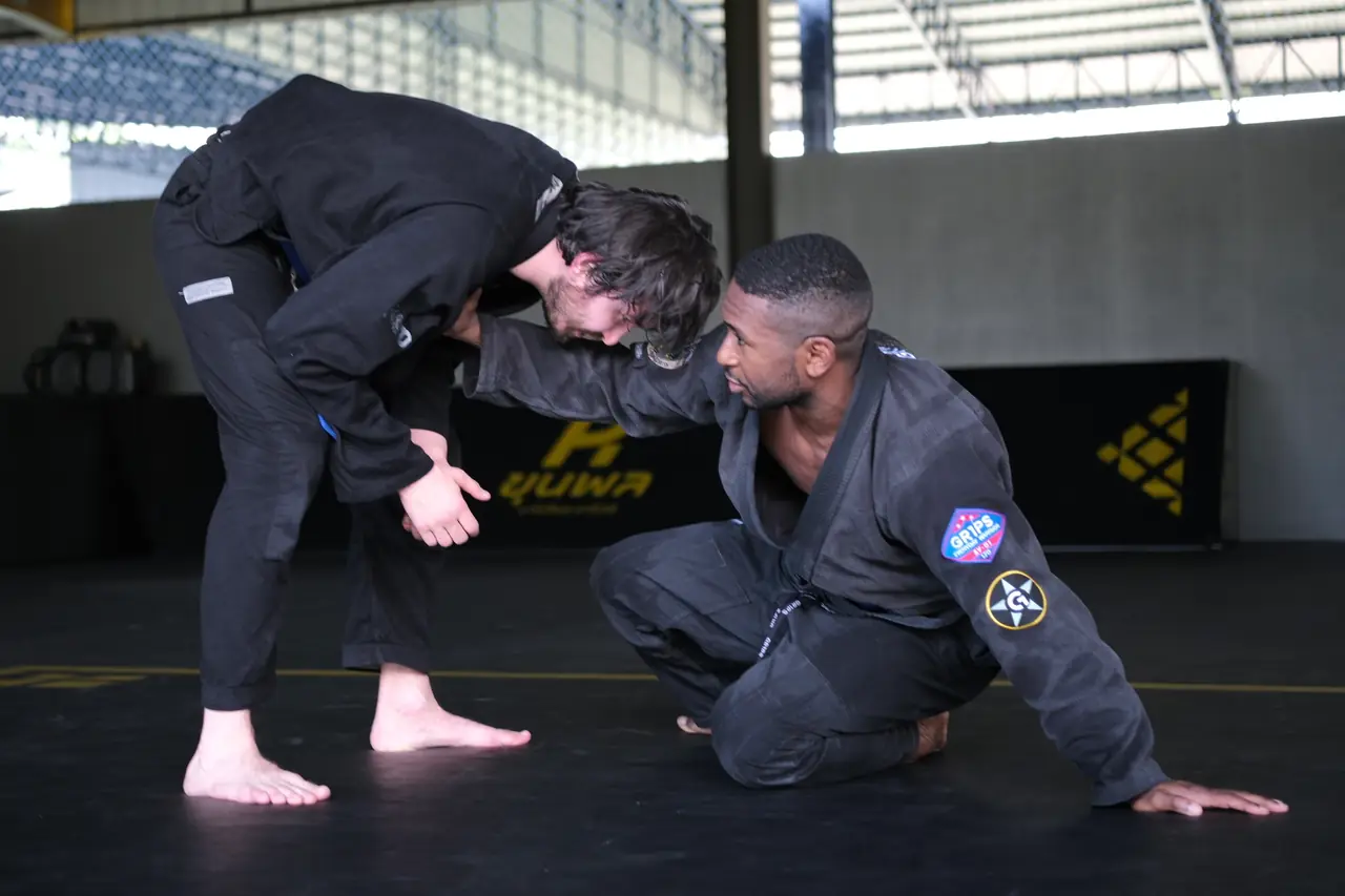 Two students in gis fight for grips at the start of a round on the Khunpon mats