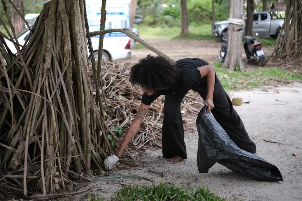 A Khunpon crew member collecting rubbish among the tree roots behind the beach