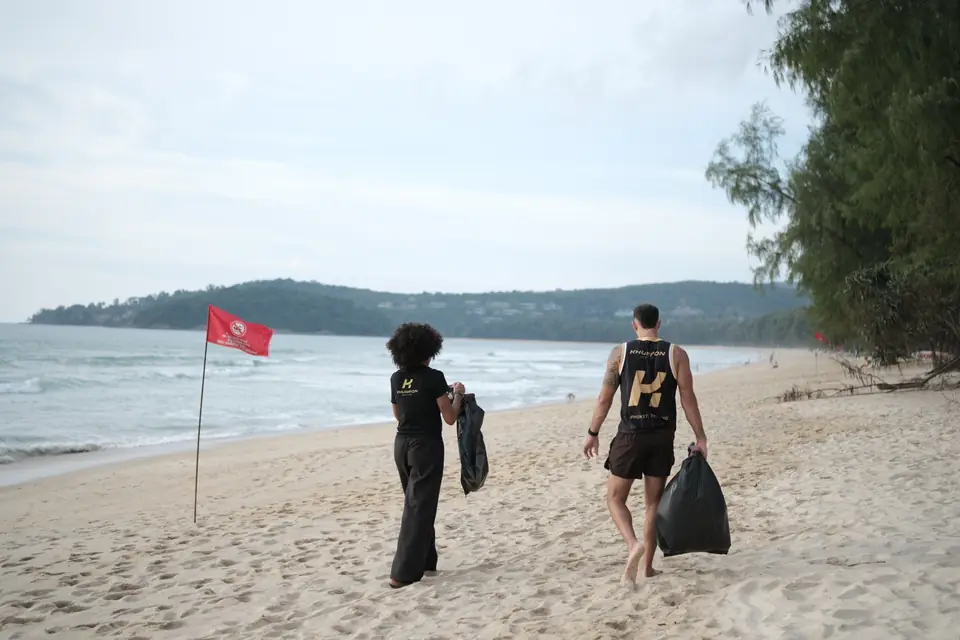 Two Khunpon crew members walking back along the beach with full rubbish bags