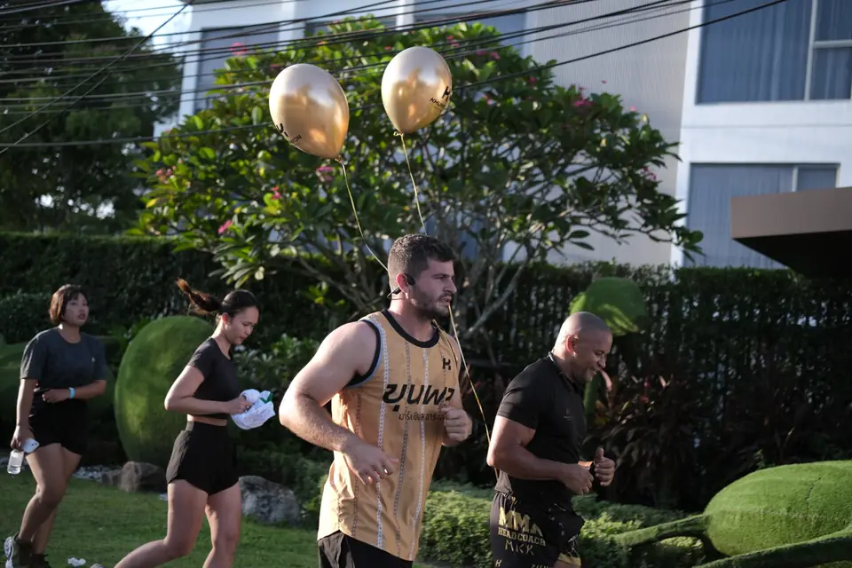 A Khunpon crew member in a gold vest running past the event gardens