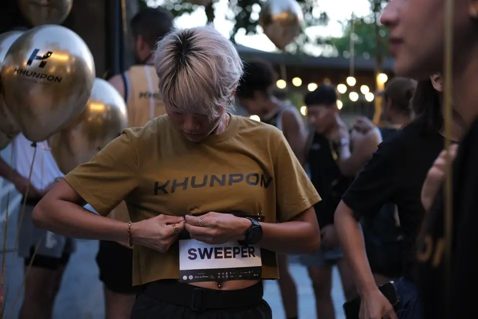 A Khunpon crew member pinning on a race bib marked Sweeper