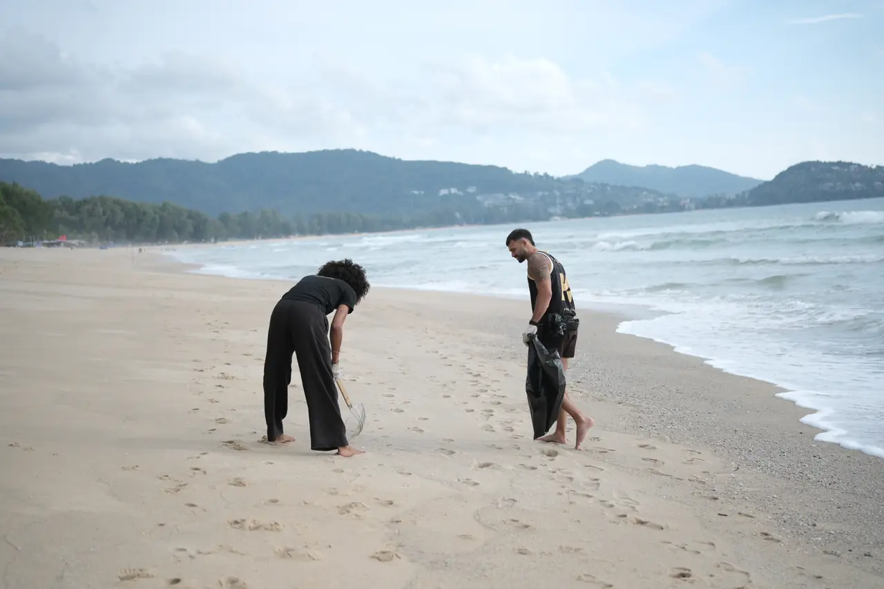 Two Khunpon crew members picking up rubbish along the shoreline at Layan Beach