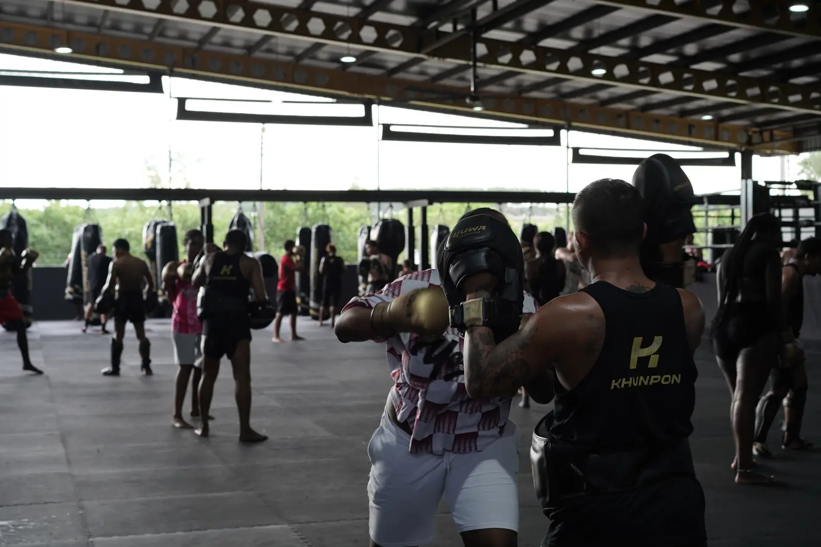 A busy afternoon at Khunpon, with coaches holding pads for students across the open-sided training floor