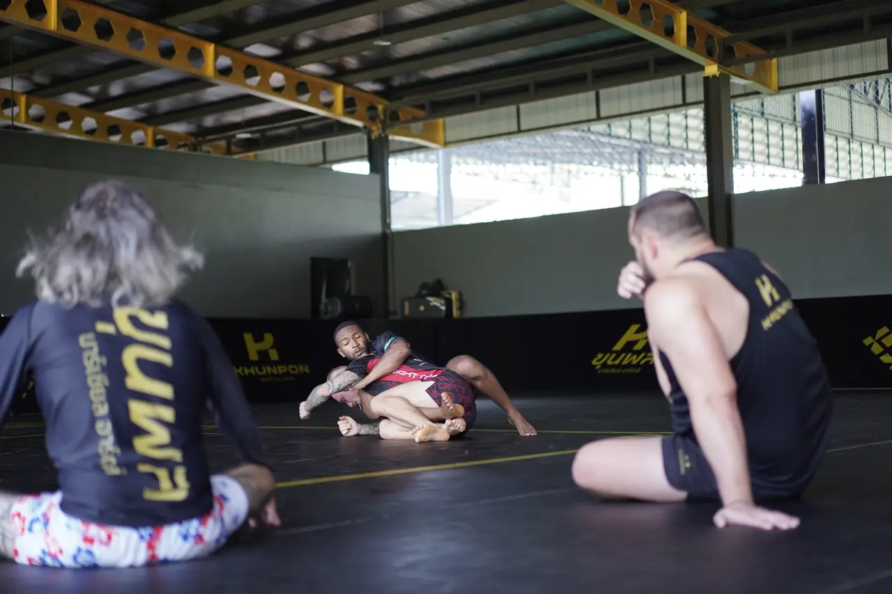 Grapplers sit at the edge of the mats watching a round in progress