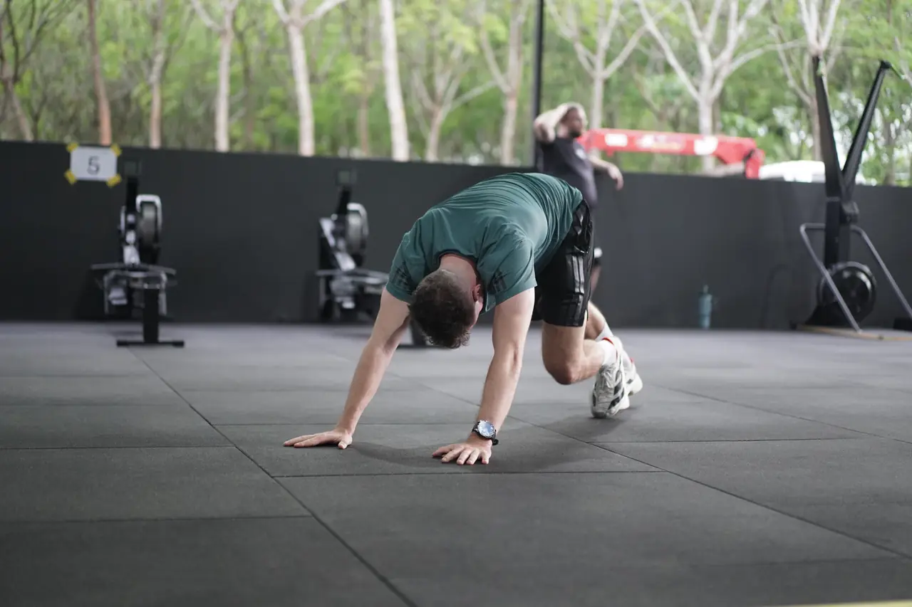 An athlete jumps forward in a burpee broad jump on the gym floor