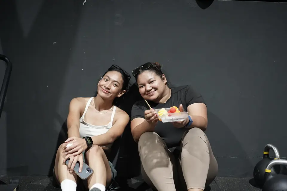 Two women sit against the wall with fruit after finishing