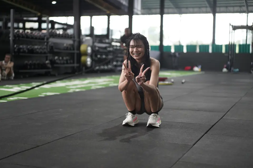 A woman crouches on the floor giving a peace sign