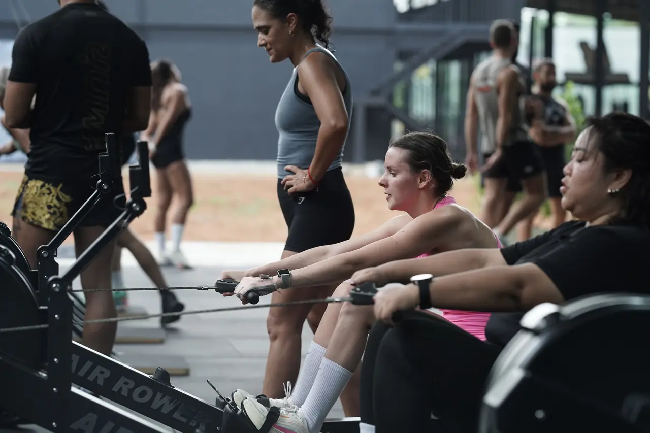 Two doubles partners sit on neighbouring rowing machines and talk between efforts