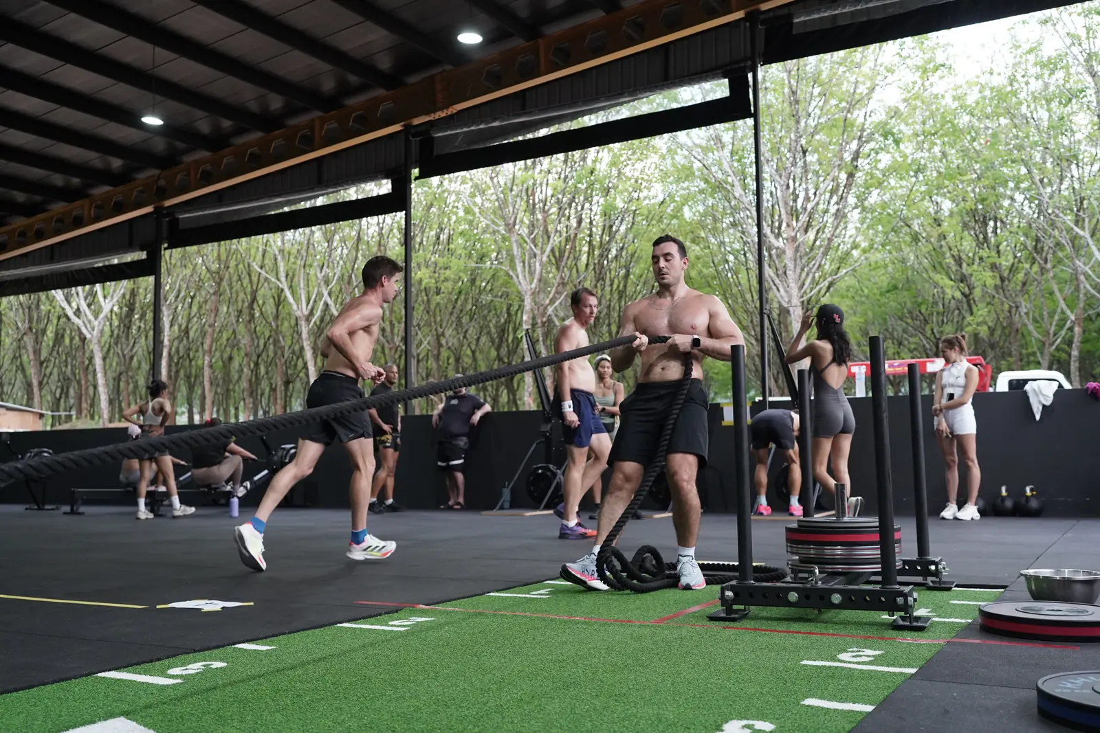 Athletes run and push sleds across the turf lanes at Khunpon during the first HYROX simulation