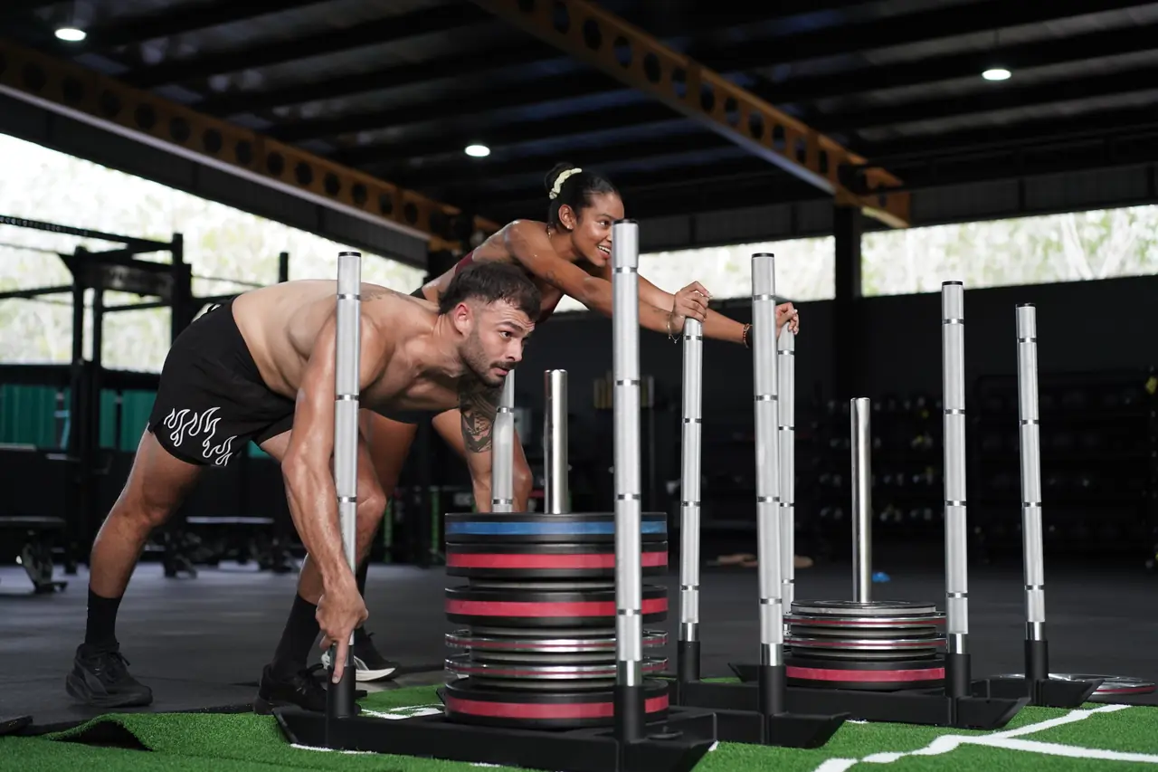 Two members push loaded sleds side by side down the green turf