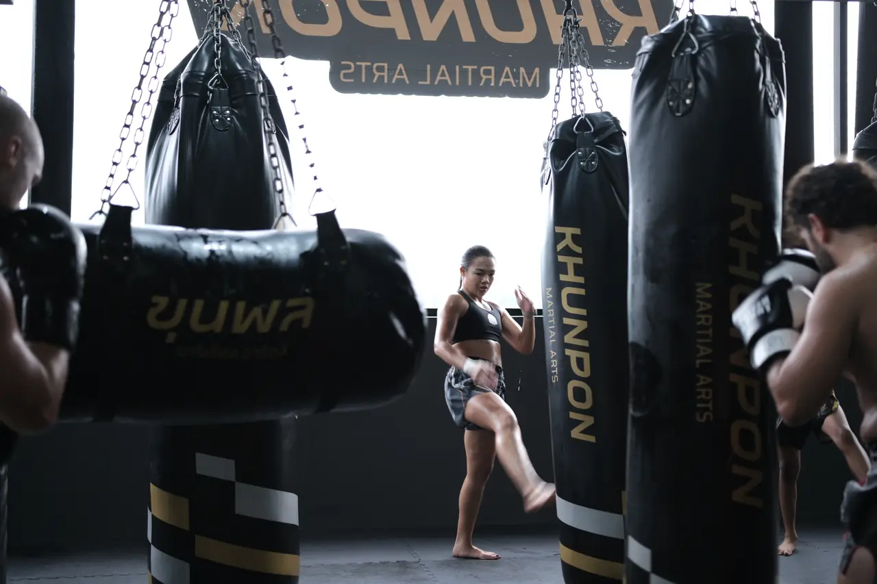 A member kicks a heavy bag in the Khunpon bag area, with KHUNPON printed down the bags