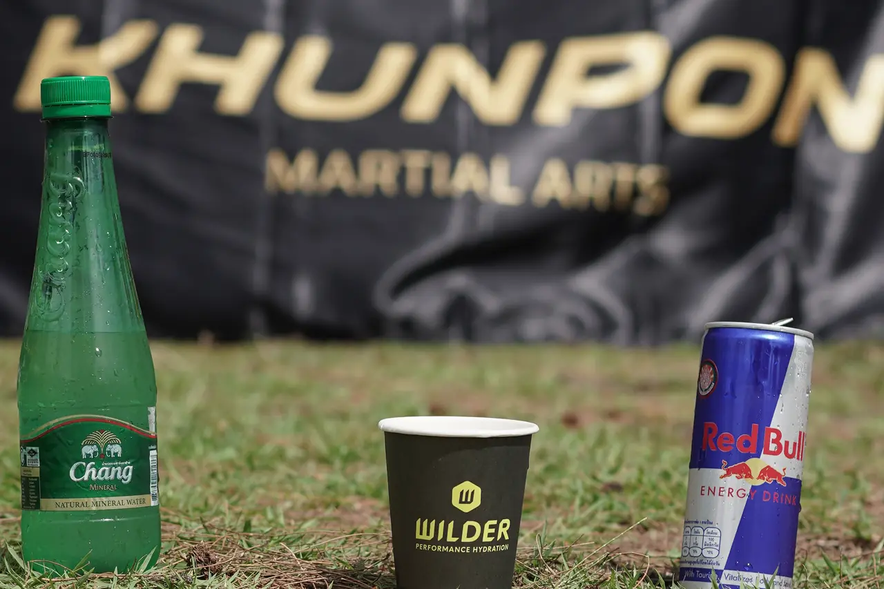 A bottle of Chang water, a WILDER cup and a can of Red Bull in front of a Khunpon Martial Arts banner