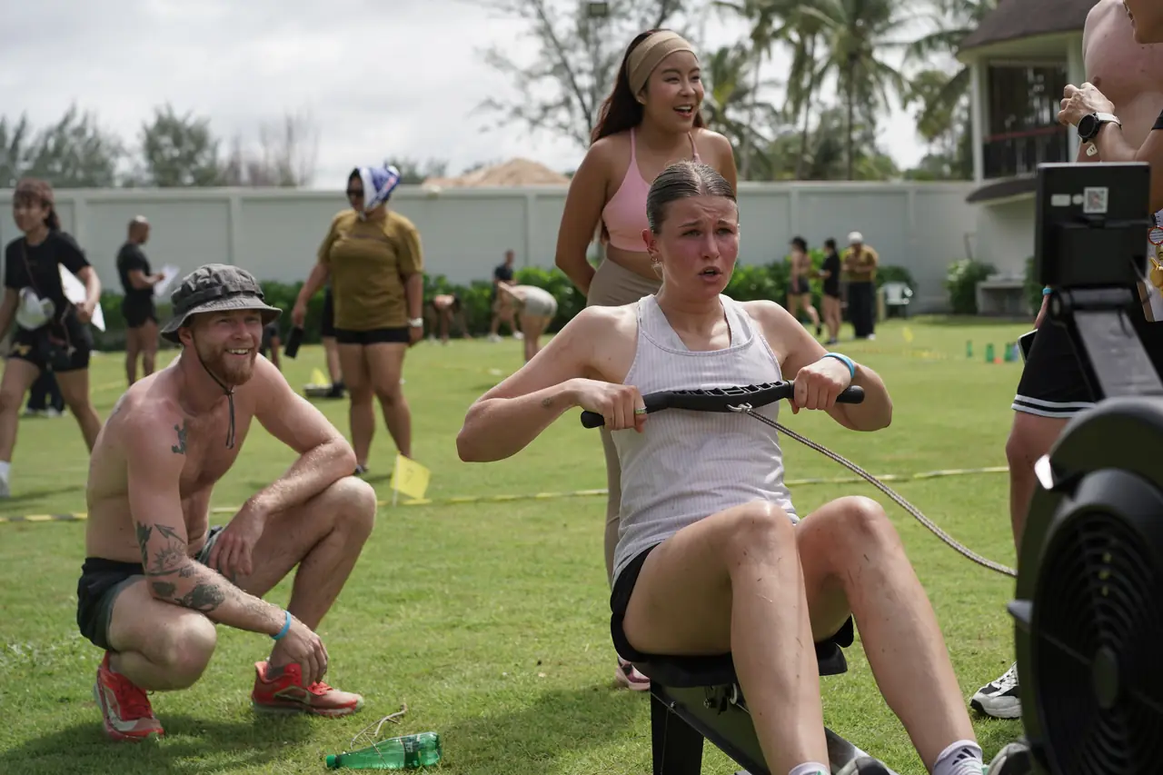 A competitor on the rowing machine while her teammate cheers beside her