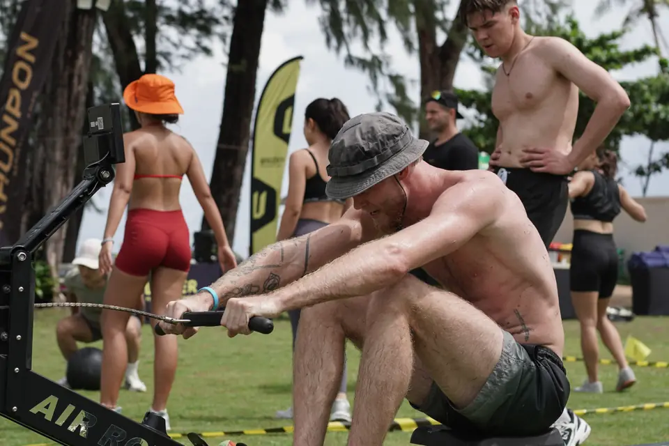 A competitor in a bucket hat pulls hard on the rowing machine
