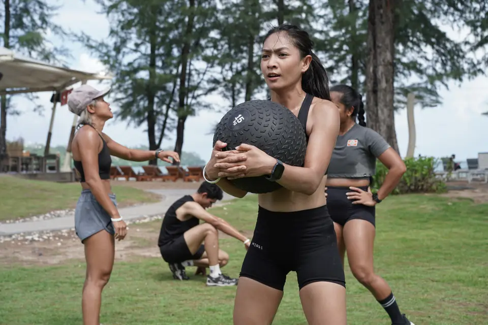 A competitor carries a slam ball at one of the eight workout stations