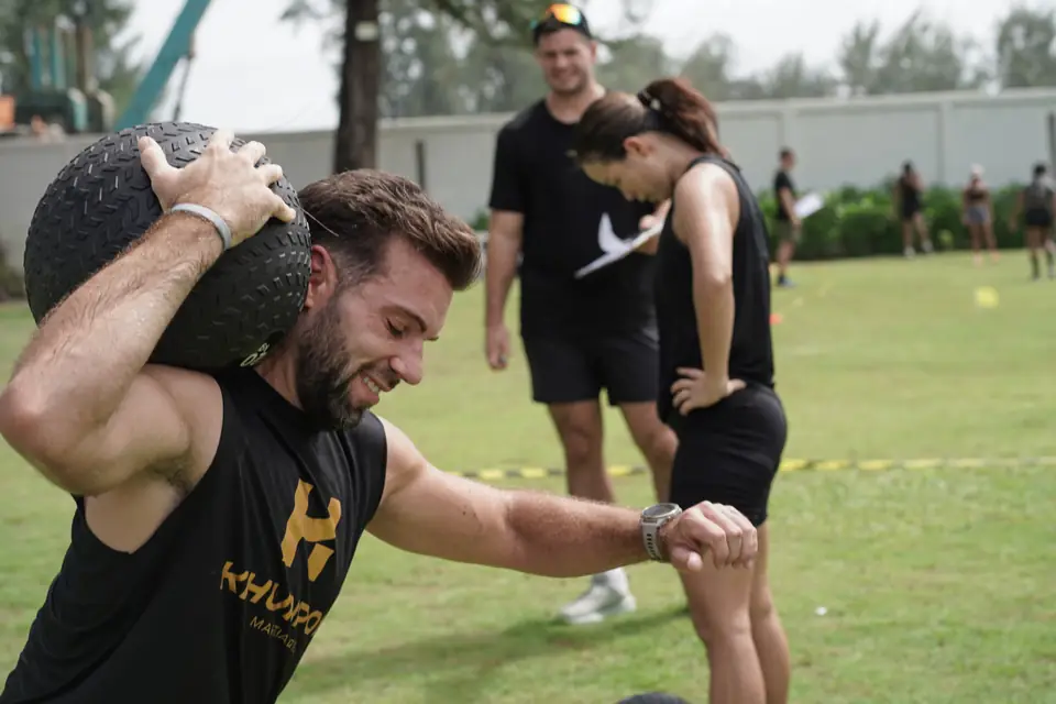 A competitor in a Khunpon vest lifts a slam ball to his shoulder