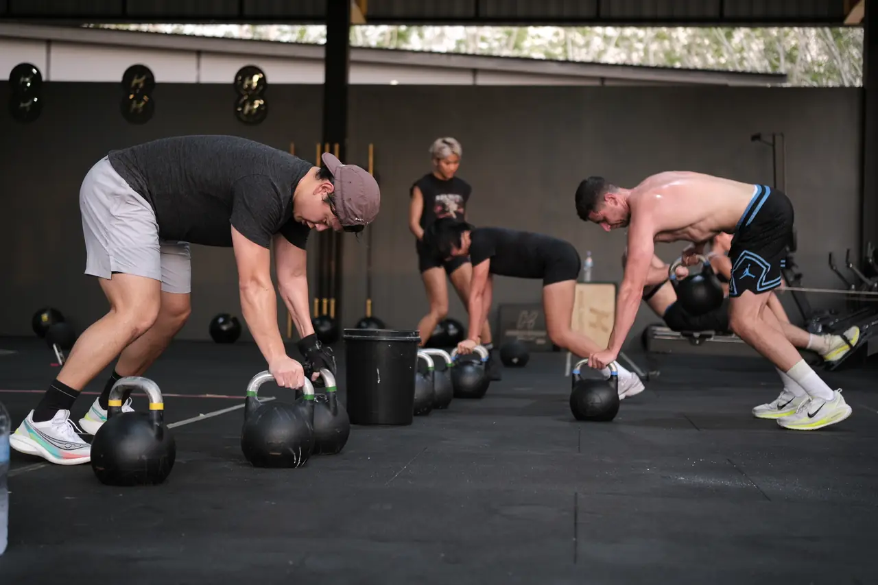Members pick up heavy kettlebells from the floor during a HYROX session