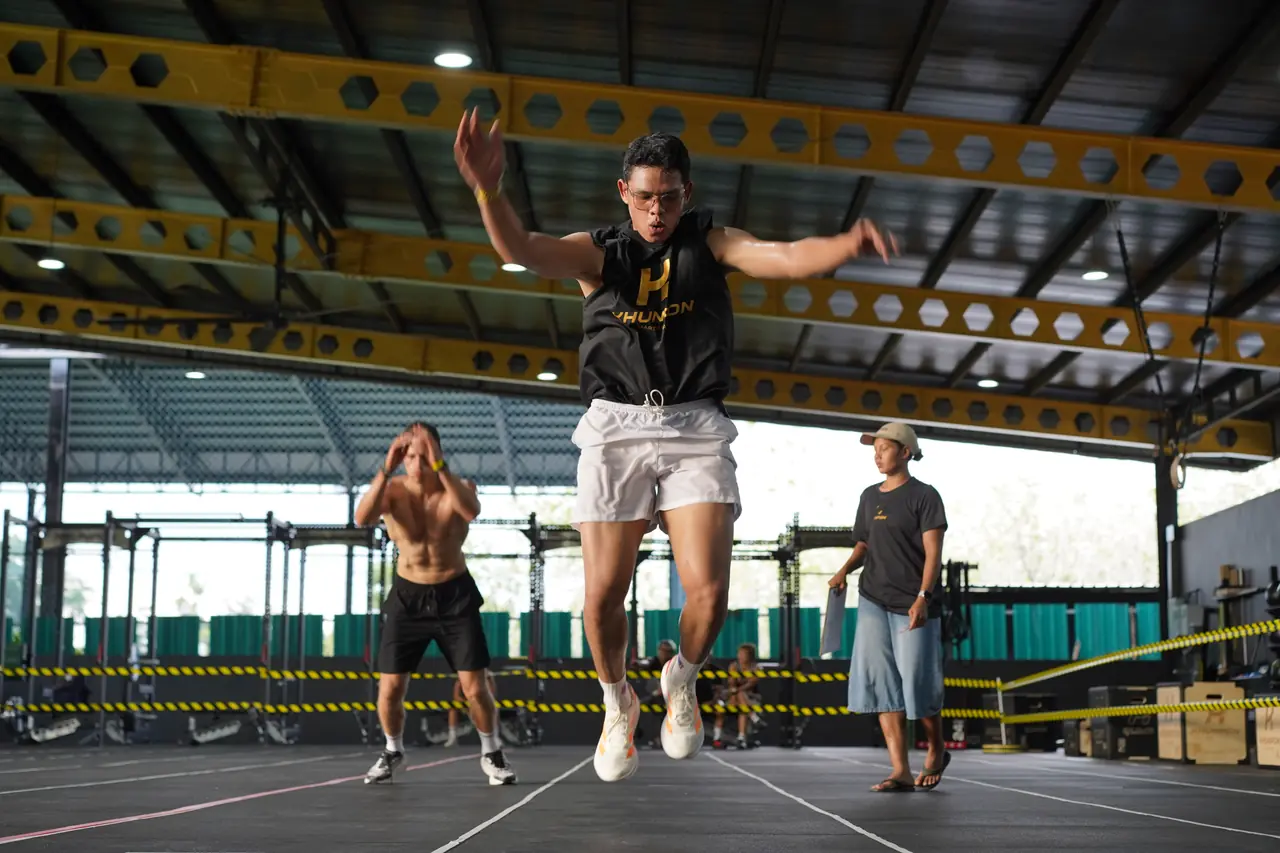 A competitor mid-air in a burpee broad jump with the gym roof above him
