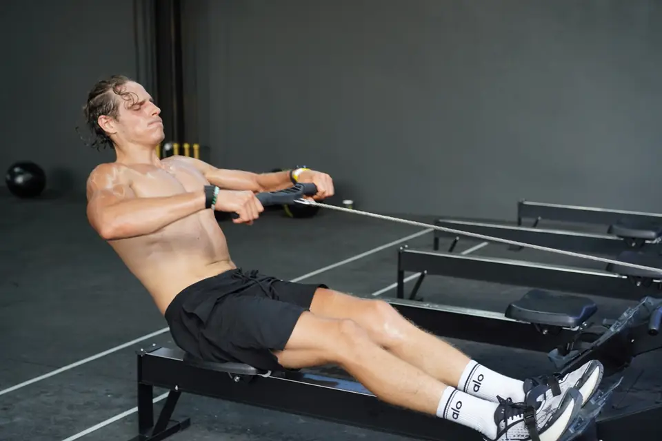 A shirtless athlete on the rowing machine at full stretch