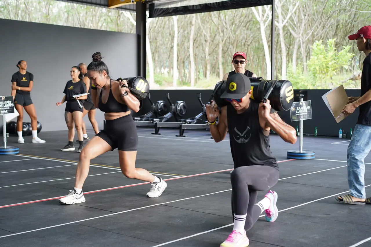 Two women carry sandbags across their shoulders through the lunge station