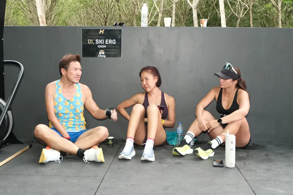 Three teammates sit against the wall under the SkiErg station sign