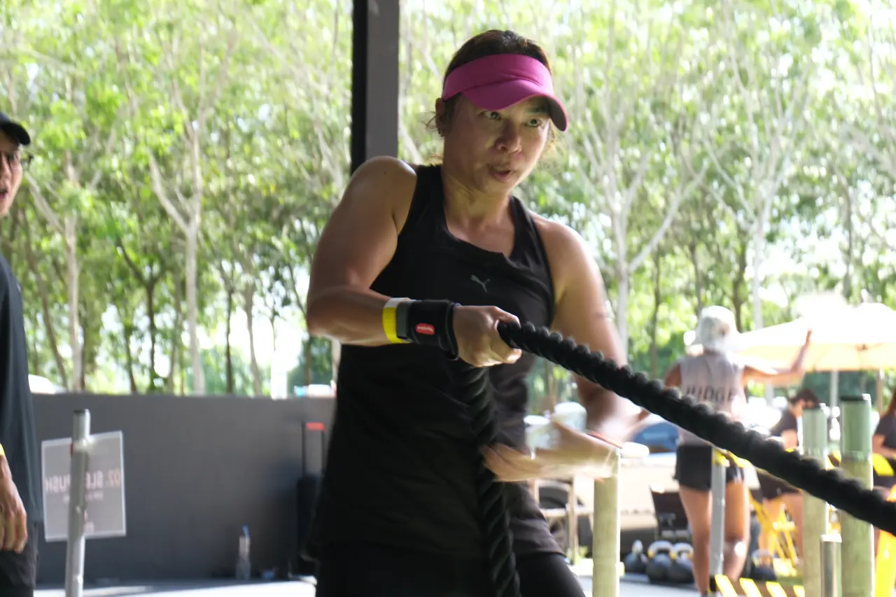 A woman in a pink visor leans back and hauls the sled-pull rope hand over hand