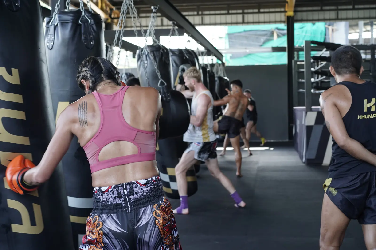 Rows of black Khunpon heavy bags hang across the training hall while members kick and punch them