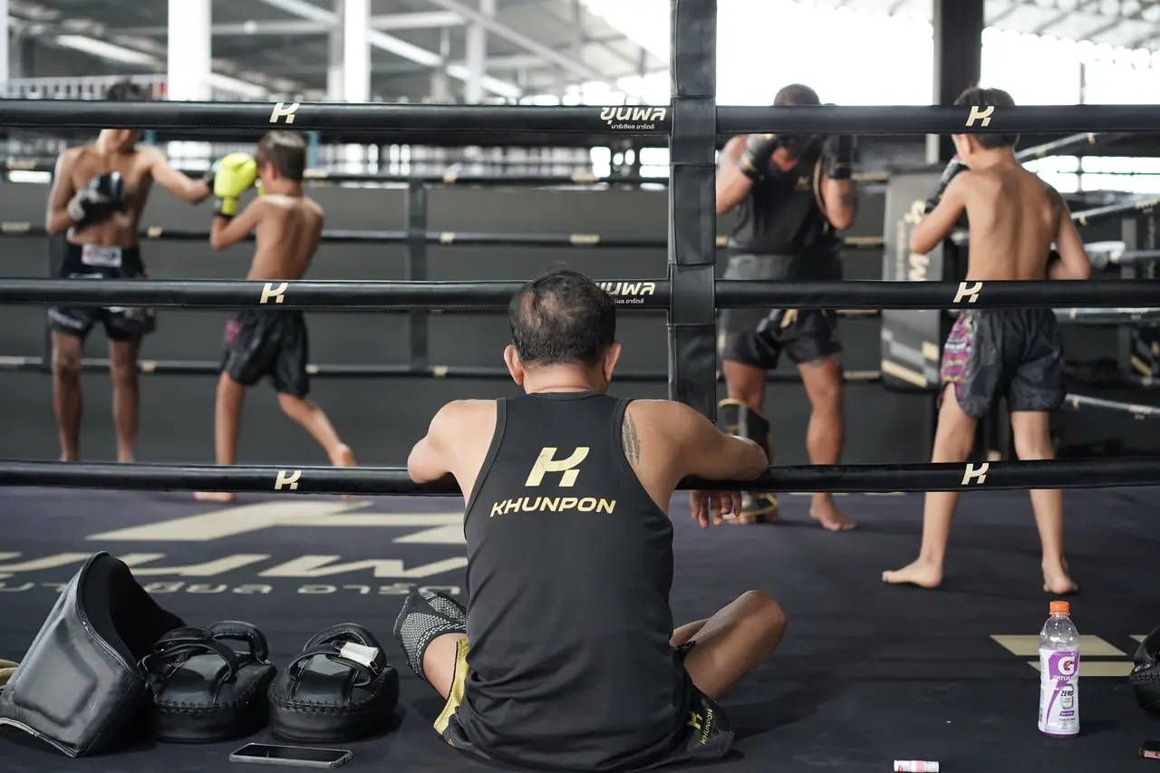 A coach sits against the ropes watching fighters shadowbox inside one of the Khunpon rings