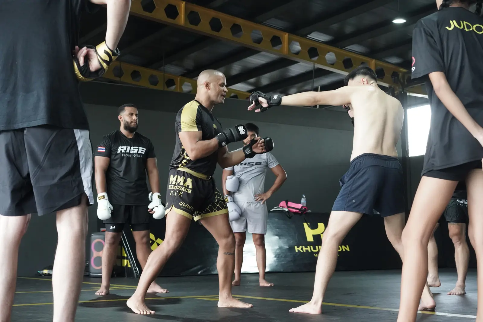Khunpon's MMA head coach works a striking exchange with a student while the class watches on the mats