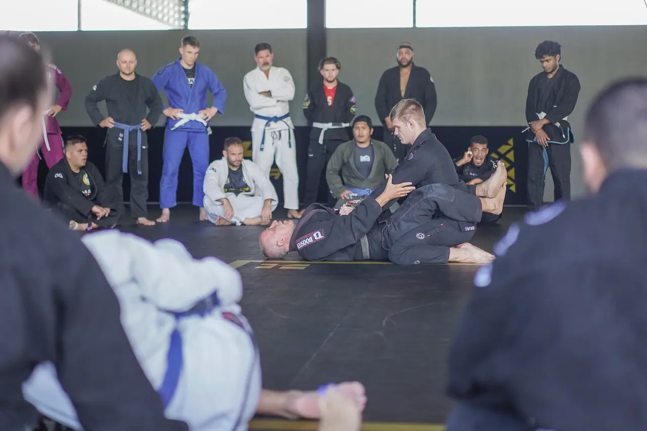 Seated practitioners watch closely as the Professor demonstrates a technique on the mat