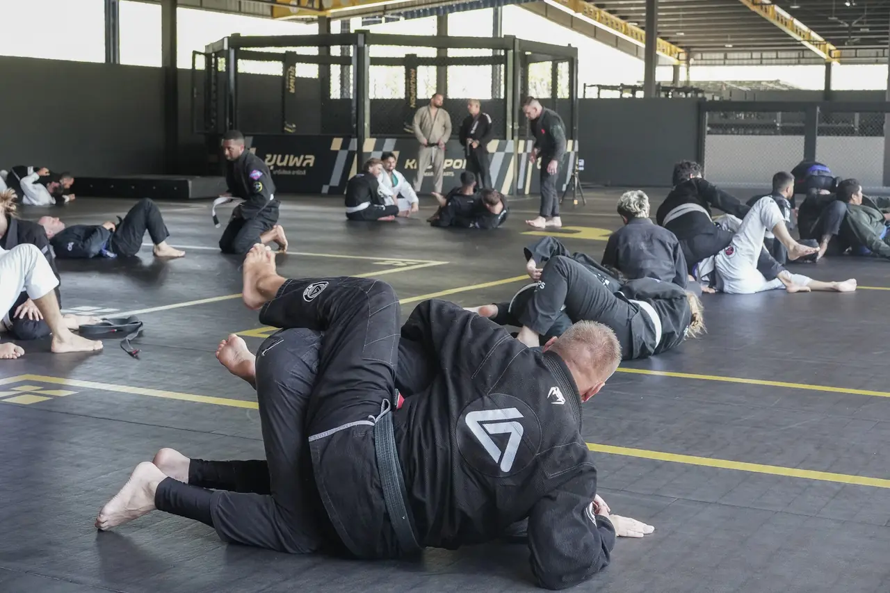 Two practitioners in black gis drill a pass on the open mat