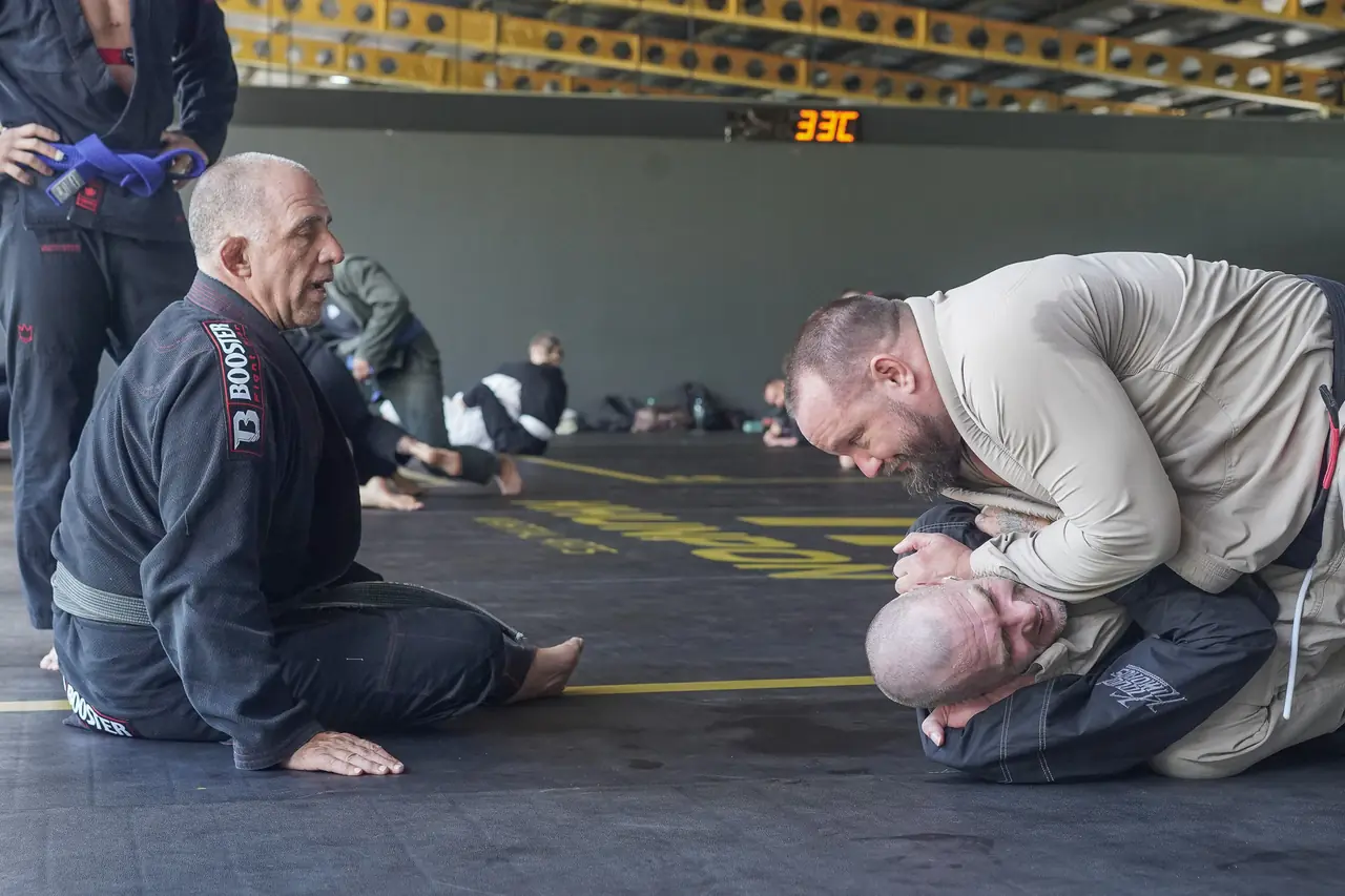 The Professor watches from the mat as two practitioners work through the technique
