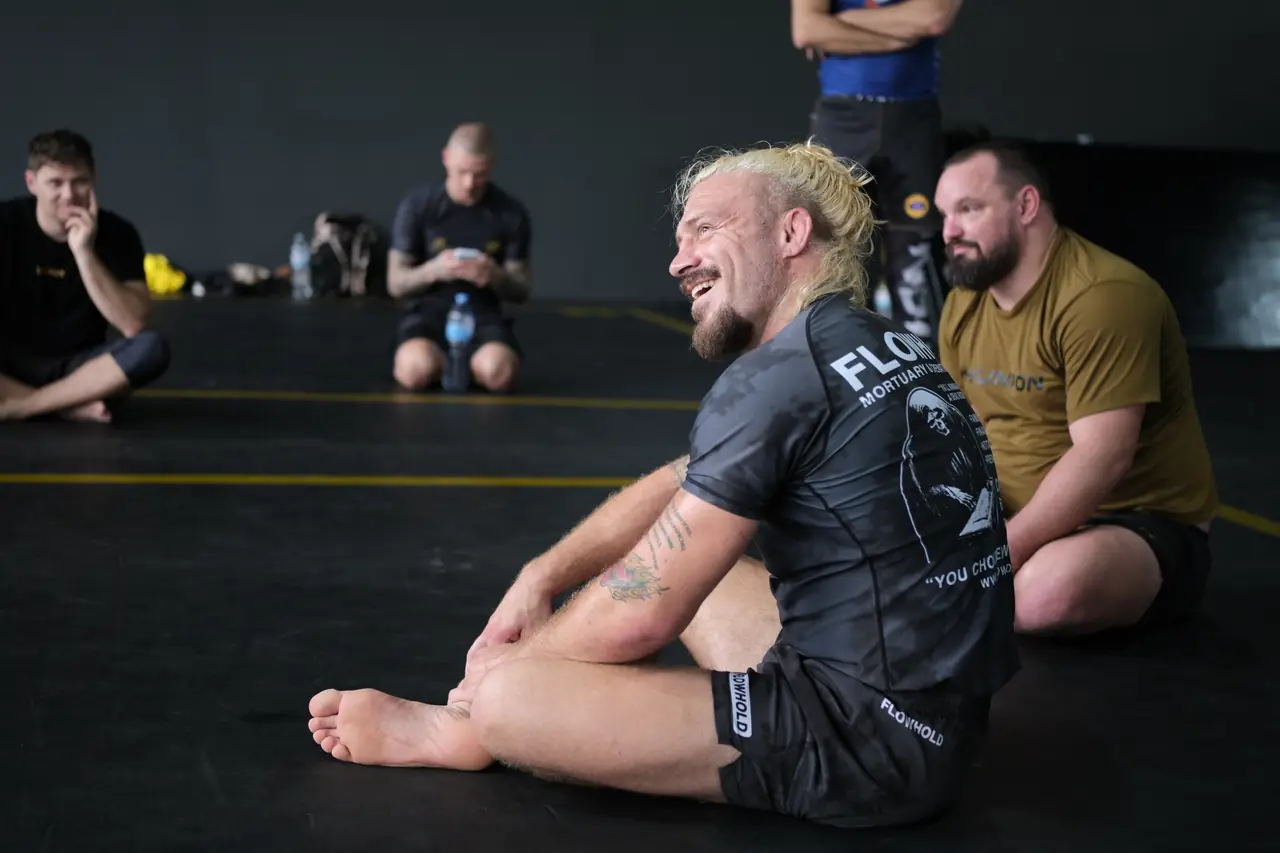 Sloan sits cross-legged on the mat, laughing, with participants around him