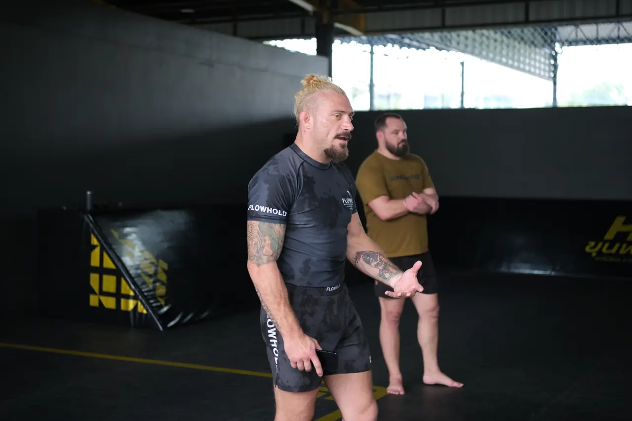 Sloan watches a pair drill from the edge of the mat, hands on hips