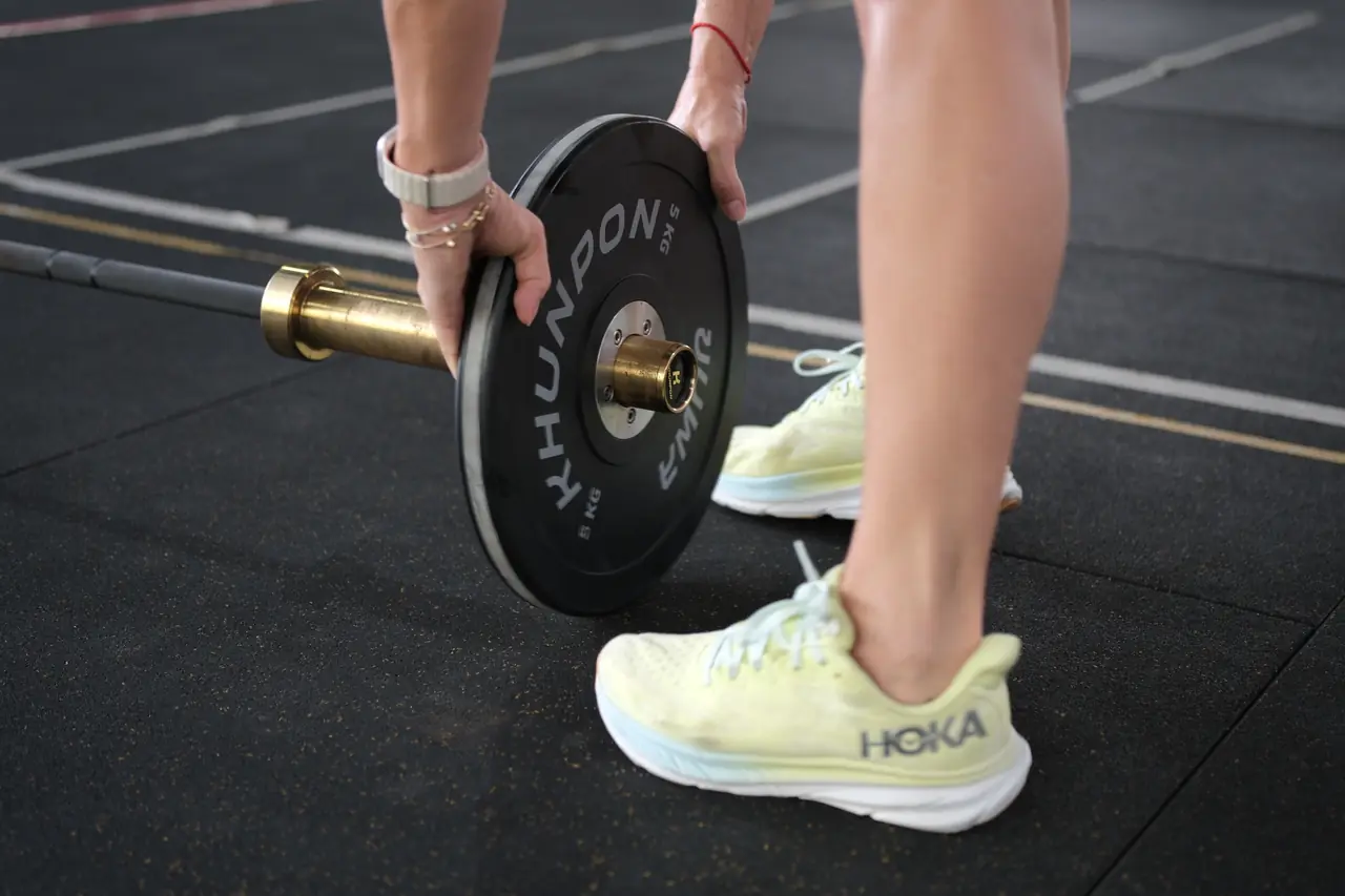 A member loads a Khunpon bumper plate onto a barbell on the gym floor
