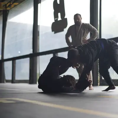 Two students roll in the gi while the coach watches