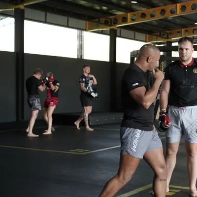 Three fighters square up in shin guards and MMA gloves