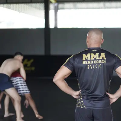 The MMA head coach watches a grappling round from the edge of the mat