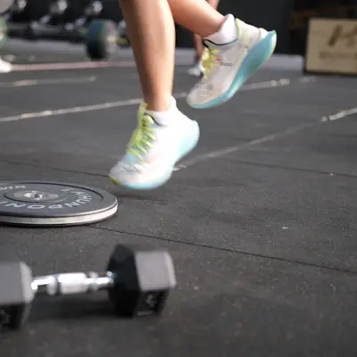 A member jumps over a weight plate on the gym floor