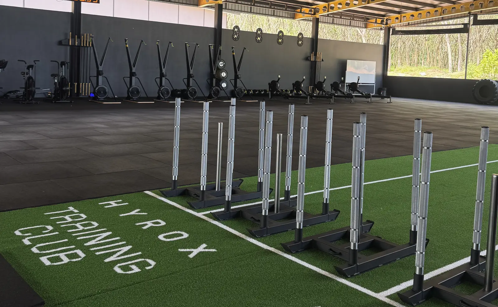 Sleds lined up on the HYROX Training Club turf, with SkiErgs, rowers and bikes along the back wall