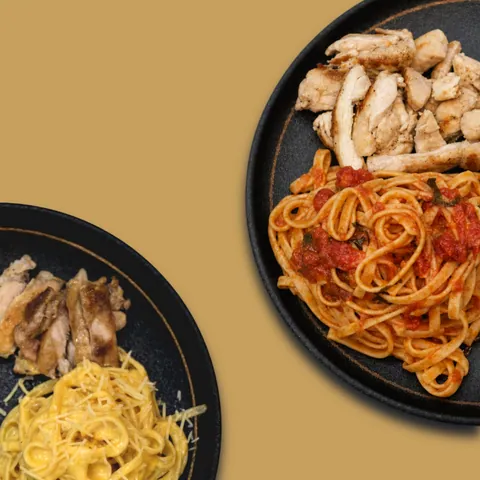 Two plates of pasta with grilled chicken, one in tomato sauce and one with a creamy sauce