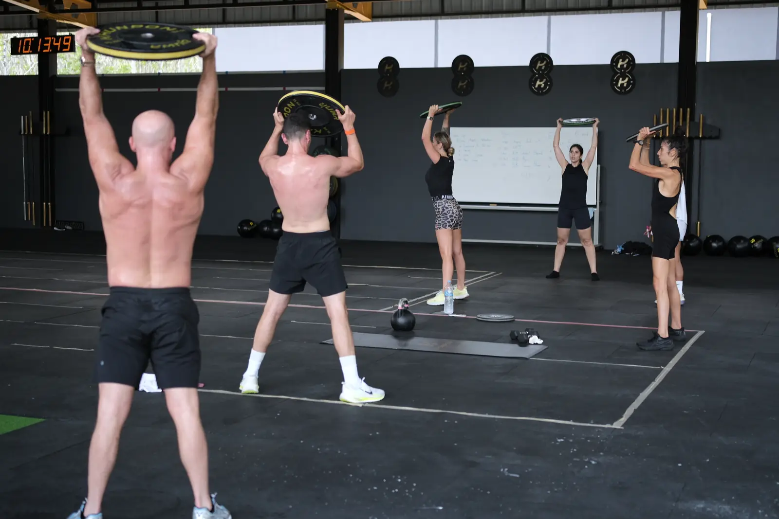 Members press weight plates overhead in a HIIT class
